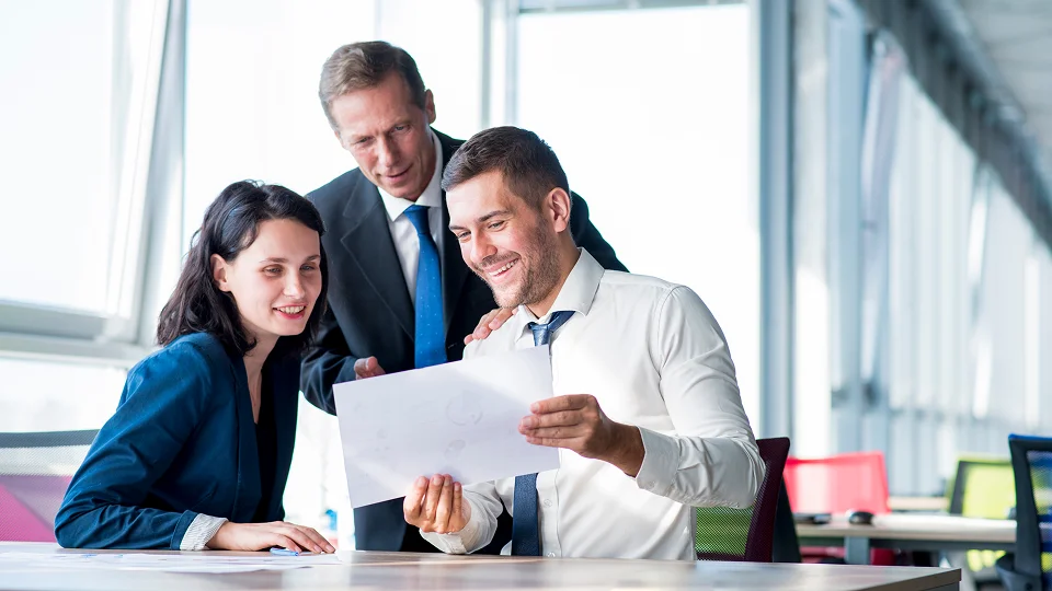 A team sits at a table smiling while reviewing a printed document together.