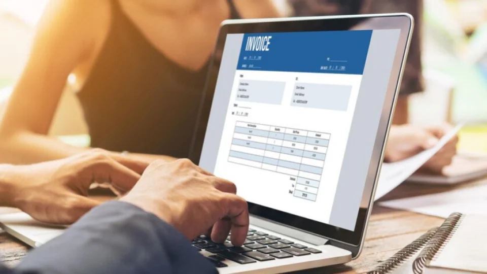 A person types on a laptop displaying an invoice template.