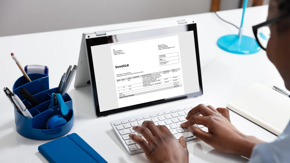 A person types an invoice email on a laptop.