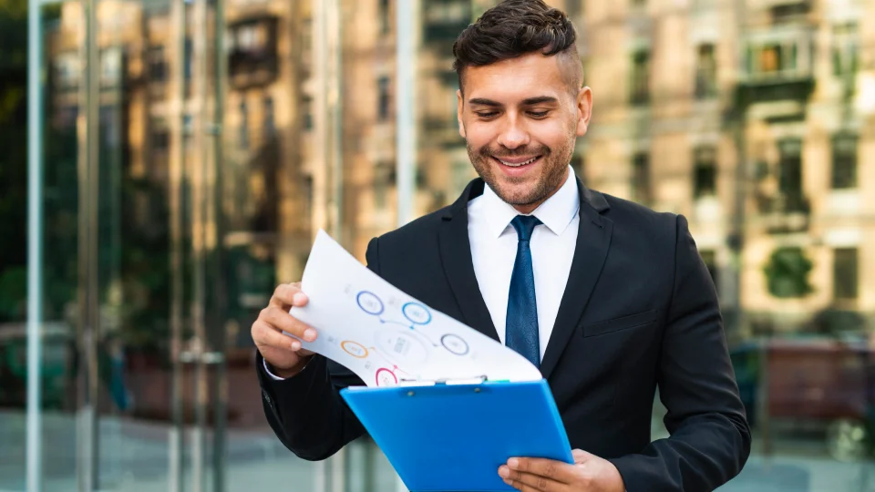 A businessman looking through business documents on a clipboard with a satisfied expression on his face.