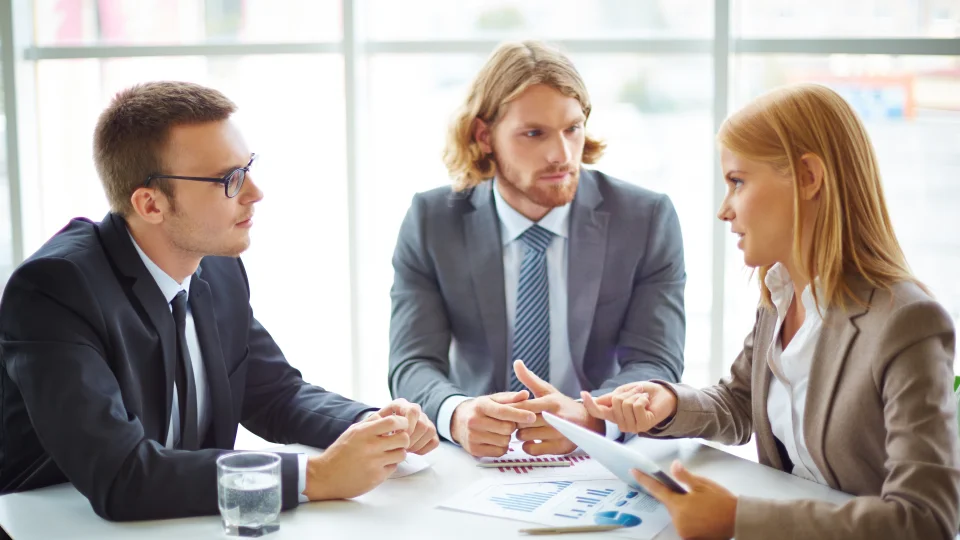 Three business professionals sit at a table, looking at financial documents and discussing different potential business formations