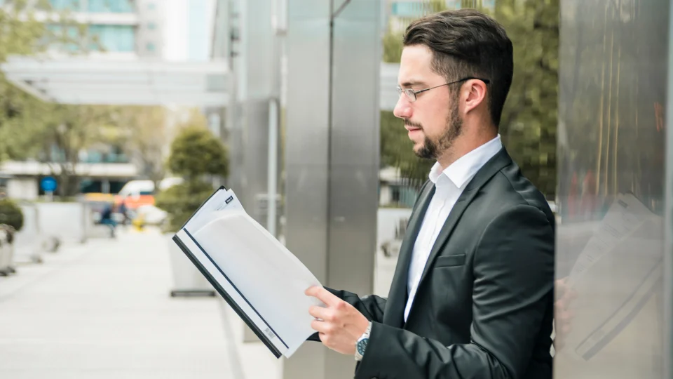A man in a suit carefully leans against a window as he reads through a job offer