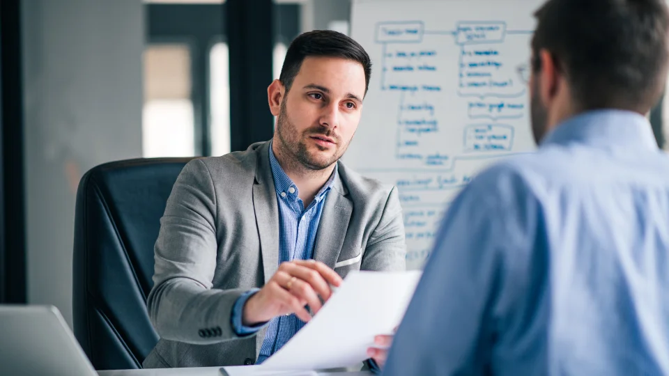 A business owner interviews a potential employee at a desk in an office.