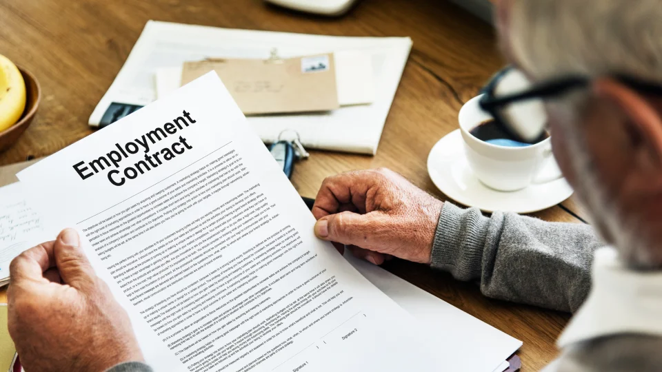 A man reads an employment contract at a table with documents and a coffee cup.