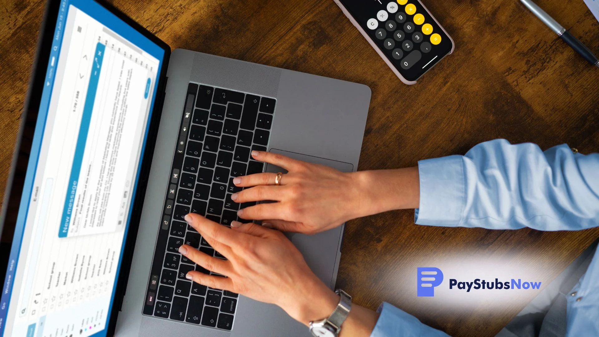 A person types on a laptop next to a calculator on a desk.