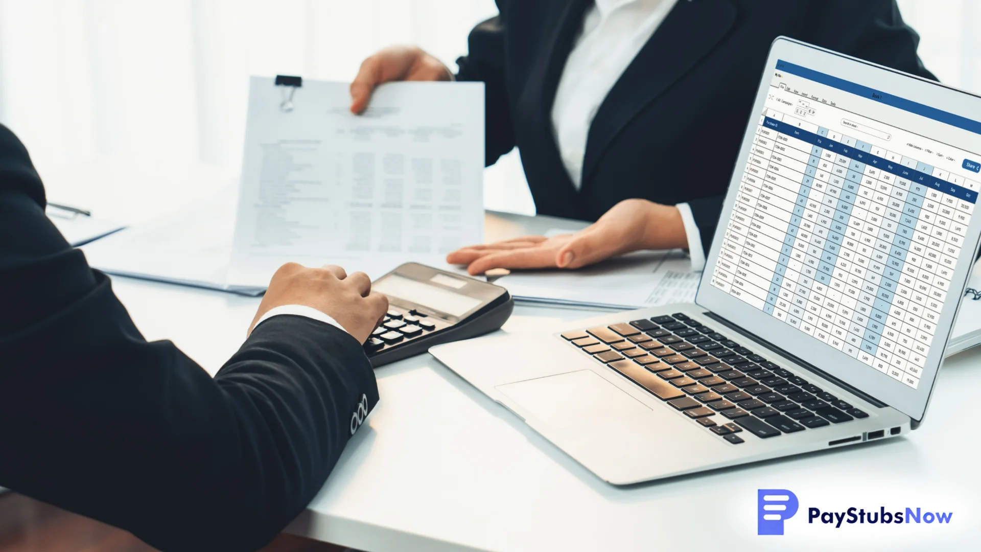 Two business professionals working together on payroll documents with a laptop showing a spreadsheet and a calculator on the desk
