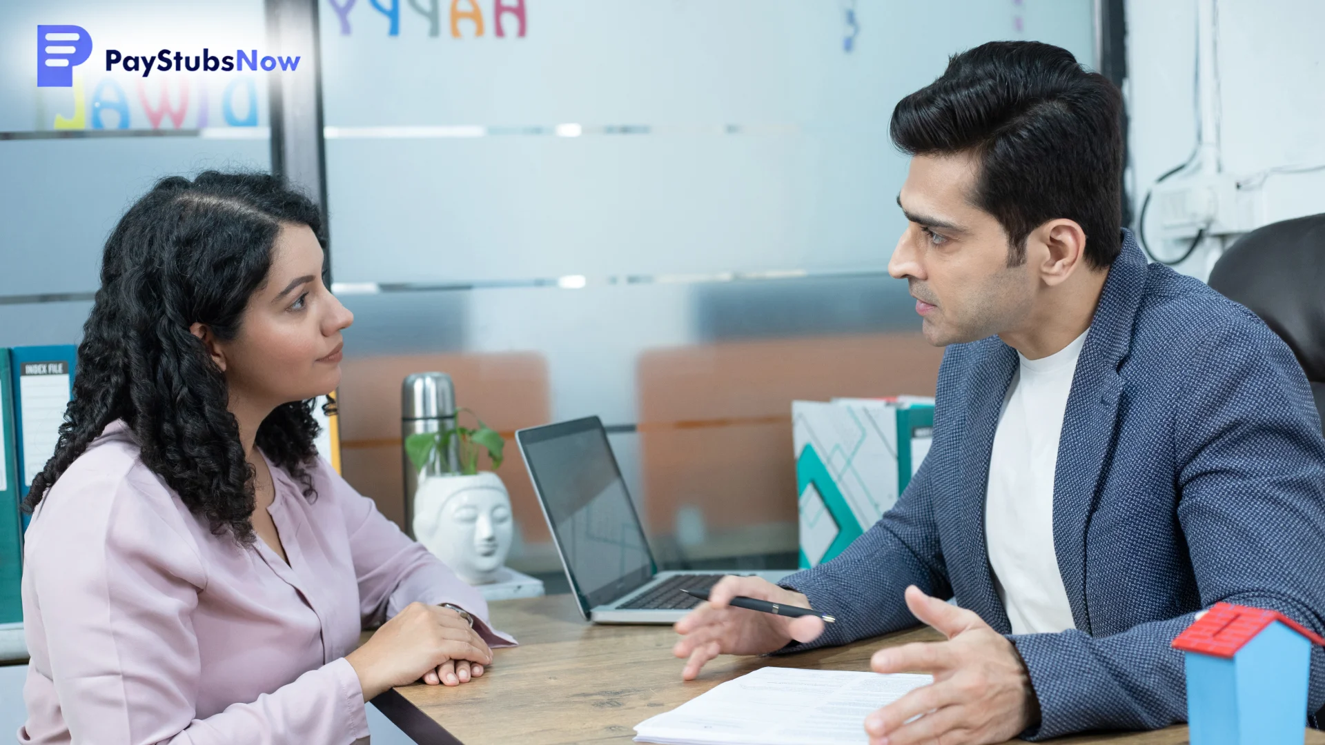 A man and a woman are seated across a desk from each other, engaged in a serious discussion.